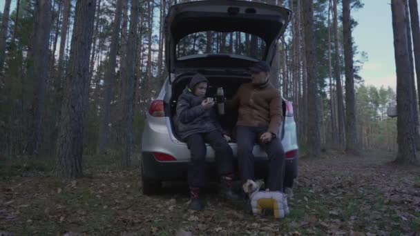 Pai e filho sentados dentro do carro tronco e beber chá de garrafa térmica. — Vídeo de Stock