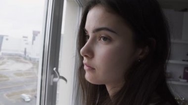 Pencere camından bakan mutsuz şirin kızın büyük ölçekli portresi.