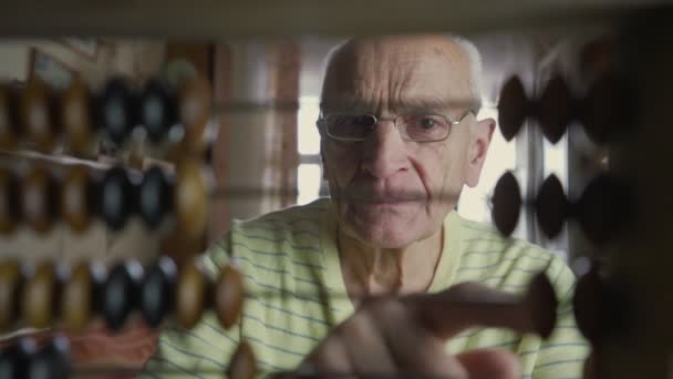 Rentner sitzt hinter antiken Abakus und rätselt über finanzielle Aufgabe. — Stockvideo