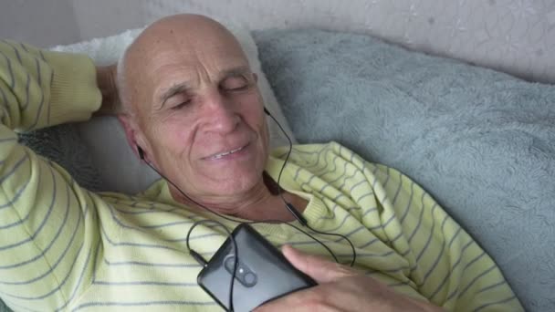 Egyedül idős férfi telefonnal a kezében és fülhallgatóval zenét hallgatva — Stock videók
