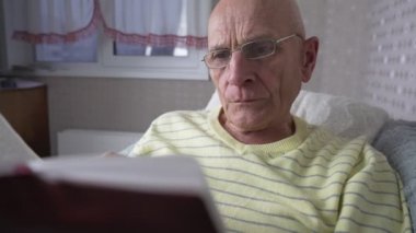 Gözlüklü, kitap okuyan ve sayfalarca kitap okuyan olgun yalnız bir adam.