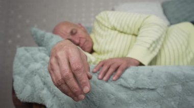 Yorgun yaşlı adam yumuşak battaniyeyle kaplı kanepede uyuyor.