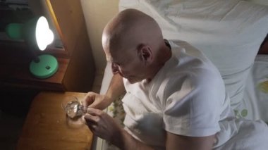 Yaşlı hasta adam hapları alıp, suyla yıkanıp, yatmaya gidiyor.