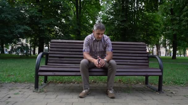 Adam, şehir parkındaki bankta oturan kol saatinin saatini kontrol ediyor. — Stok video