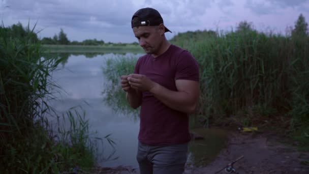 Samec rybář stojící na břehu jezera váže návnadu na vlasec — Stock video