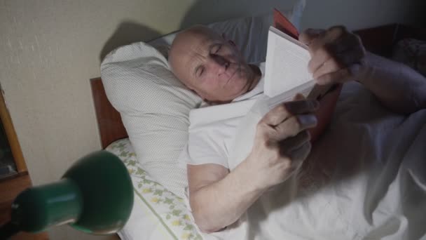 Sozinho velho avô deitado na cama à noite e lendo livro — Vídeo de Stock