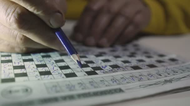 Pensioner in yellow hoodie fills out crossword puzzle using pencil — Stock Video