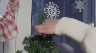 Küçük yeşil Noel ağacını süsleyen genç kız pencere eşiğinde duruyor..