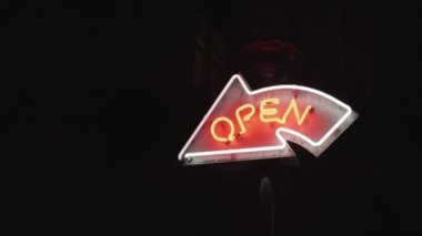 Gece şehir caddesinde bar veya dükkan girişinin yanında açık ok neonu işareti.