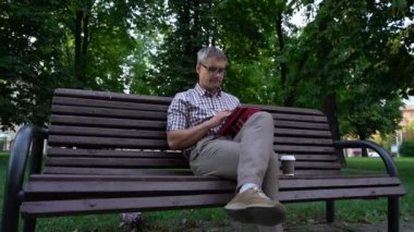 Adam tablette çalışıyor, bankta oturuyor, elinde kahveyle.