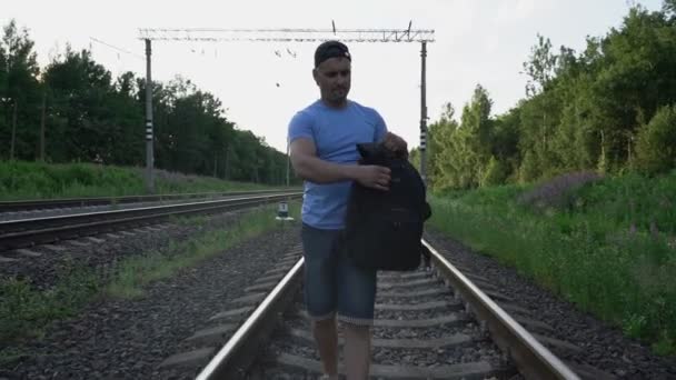 Uomo adulto cammina lungo rotaie di ferrovia e mette sullo zaino — Video Stock