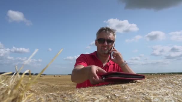 Man near straw bale finishes talking on mobile phone and working in tablet — Stock Video