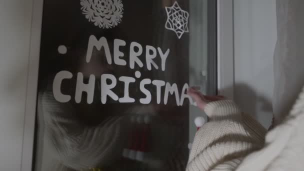 Lány tartja papír levél a kezében, és ragasztó Boldog karácsonyi szöveget az ablakon — Stock videók
