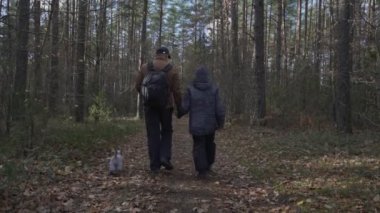 Baba oğul orman yolunda yürüyor ve el ele tutuşuyorlar.