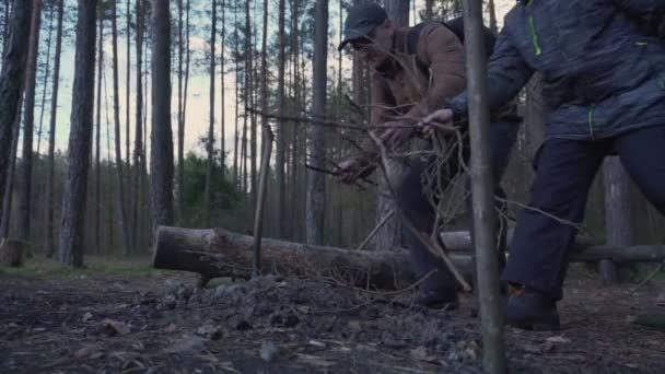 Vuxen man och ung pojke lägger ner penselträpinnar i lägerelden — Stockvideo