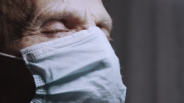 Rostro de un anciano serio cubierto de mascarilla médica que abre los ojos con miedo. — Vídeos de Stock