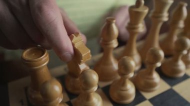 Büyük, olgun bir adam elinde bir satranç taşı tutuyor ve hamle yapıyor..