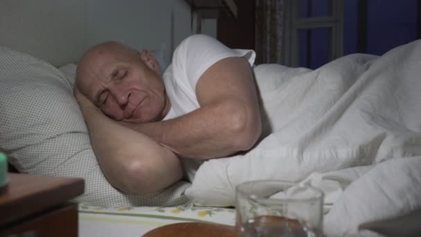 Ηλικιωμένος ασθενής ξαπλωμένος στο κρεβάτι με χάπια και ένα ποτήρι νερό σε πρώτο πλάνο — Αρχείο Βίντεο