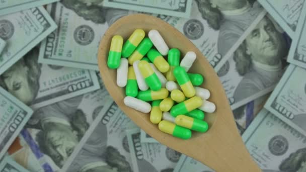 Tabletas médicas blancas y verdes en cuchara de madera contra dólares — Vídeo de stock