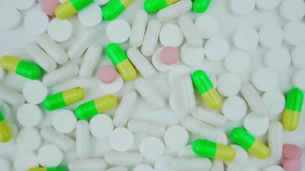 Bílé a vícebarevné pilulky otáčet na bílém pozadí horní pohled. — Stock video