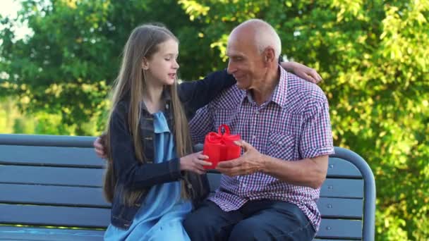 Petite-fille donne boîte cadeau rouge à l'homme âgé sur le banc — Video