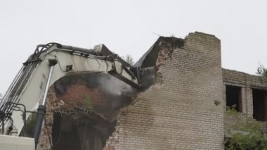 Büyük demir kepçeli buldozer beyaz tuğla duvarlı antika bir bina kazıyor..