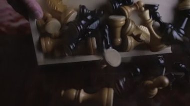 Yetişkin satranç oyuncusu eğiliyor, satranç tahtası eğiliyor ve taşlar tahta masaya düşüyor.