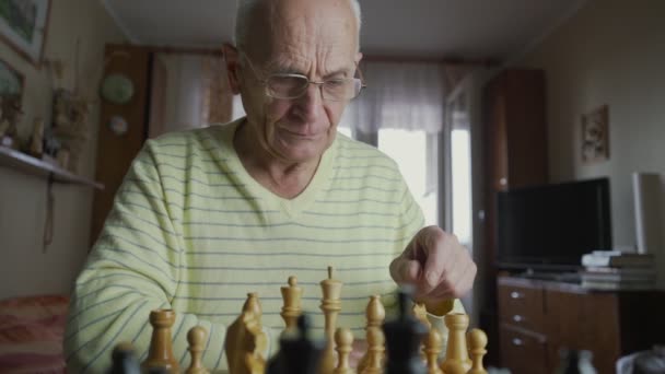 У віці сіро-волохатий чоловік в окулярах рухає єпископську частину на шаховій дошці — стокове відео