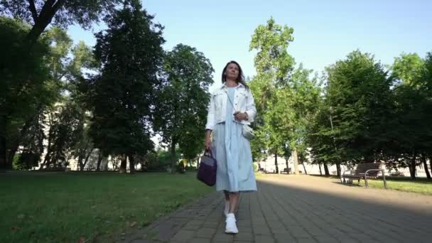 Middle aged woman in long light dress and white jacket walks — 图库视频影像