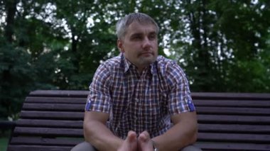 Adam şehir parkındaki ahşap bankta otururken etrafına bakıyor.