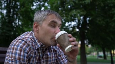 Gri saçlı adam kahvesini yudumluyor. Şehir parkında havanın tadını çıkarıyor.