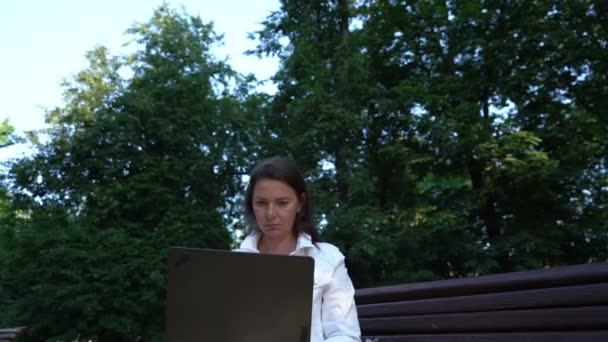 Beyaz ceketli kadın, yeşil parktaki bilgisayarda çalışıyor. — Stok video