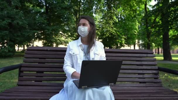 Žena středního věku v masce pracuje na počítači sedí v parku — Stock video