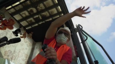 Tıbbi maskeli erkek kazıcı sürücüsü kazıcı kollarını kontrol ediyor