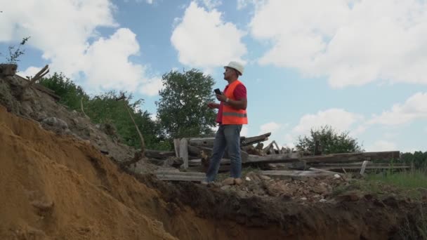 Předák stojí na okraji zákopu a dává pokyny pro řidiče bagru — Stock video