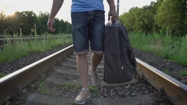 Hombre en pantalones cortos y jersey azul camina lentamente a lo largo de rieles de ferrocarril vista cercana — Vídeos de Stock