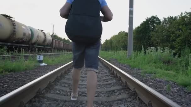 Man loopt langs rails van spoorweg naast passerende trein en draagt gitaar — Stockvideo