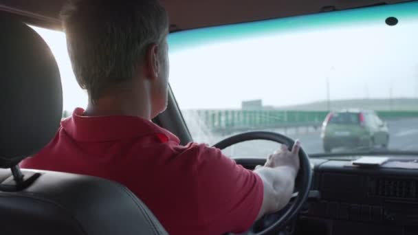 Συμπυκνωμένος άνθρωπος σε κόκκινο φανέλα οδηγεί αυτοκίνητο στην εθνική οδό το καλοκαίρι — Αρχείο Βίντεο