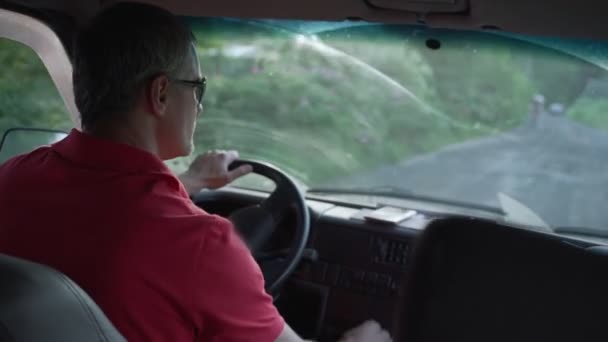 Hombre en gafas de sol conduce a lo largo de camino de tierra en minivan — Vídeos de Stock