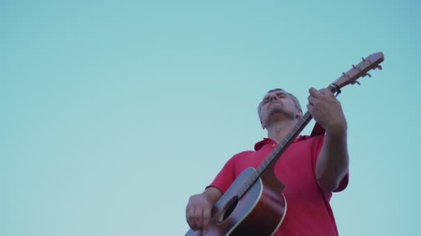 Homem autêntico toca guitarra corda acústica contra céu azul claro — Vídeo de Stock