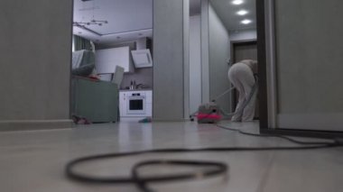 Evde elektrikli süpürgeyle ahşap döşemeyi temizleyen orta yaşlı bir kadın.