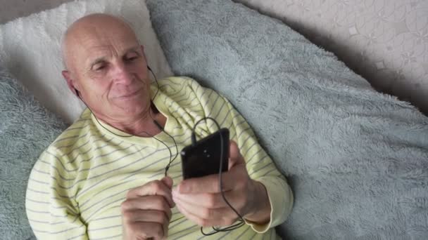Aged man listening music with headphones on record smartphone player — Stockvideo