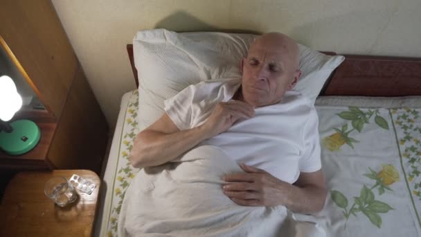 Sick senior man in agonize lying in bed at night near stand with pills — Stock Video