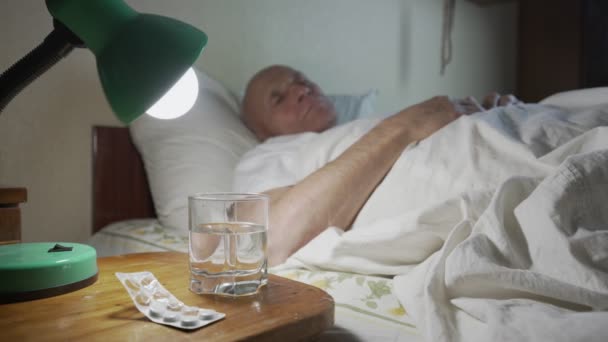 Anciano enfermo acostado en cama de hospicio con luz eléctrica de la lámpara — Vídeos de Stock