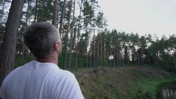 Man stands on edge of cliff near river raises his hands to sky — Stock Video