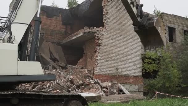 Heavy caterpillar excavator driving along demolishing ruins of old house — ストック動画