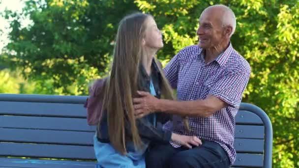 Happy teenage girl comes to hug grandfather sitting on bench — Stockvideo