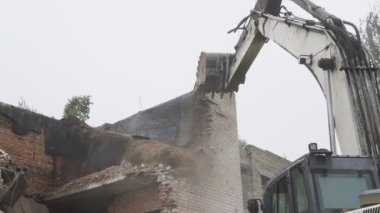 Ağır buldozer beyaz tuğla duvarlı eski binayı yıkıyor.