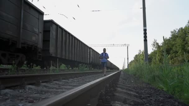 Άτομο ταξιδιώτη με σακίδιο βόλτες κατά μήκος των σιδηροτροχιών κοντά διερχόμενο τρένο — Αρχείο Βίντεο
