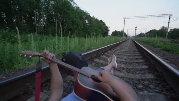 Hombre se encuentra en traviesas de ferrocarril toca la guitarra y canta fuera de la ciudad — Vídeo de stock